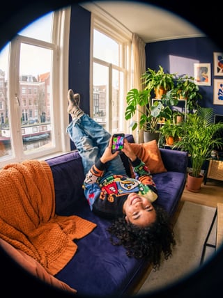 Hand houdt smartphone vast met streamingvideo in een warme woonkamer